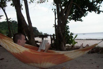 Charles Kosman reading a book in a hammock by the ocean
