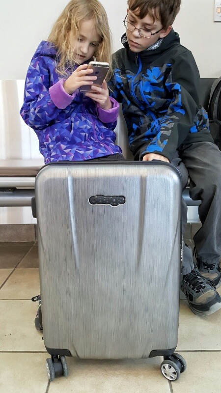 eBags Allura 22 hardside handbagage met geborsteld stalen look en onze kinderen op de luchthaven