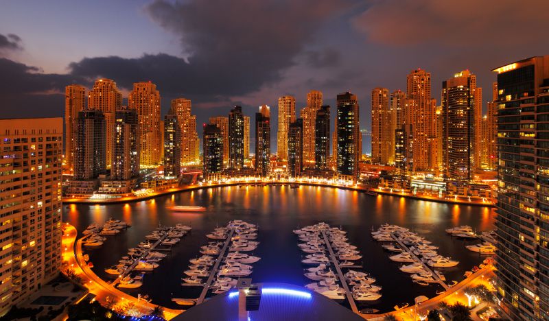 Dubai Marina de noche con pasarelas iluminadas y barcos anclados