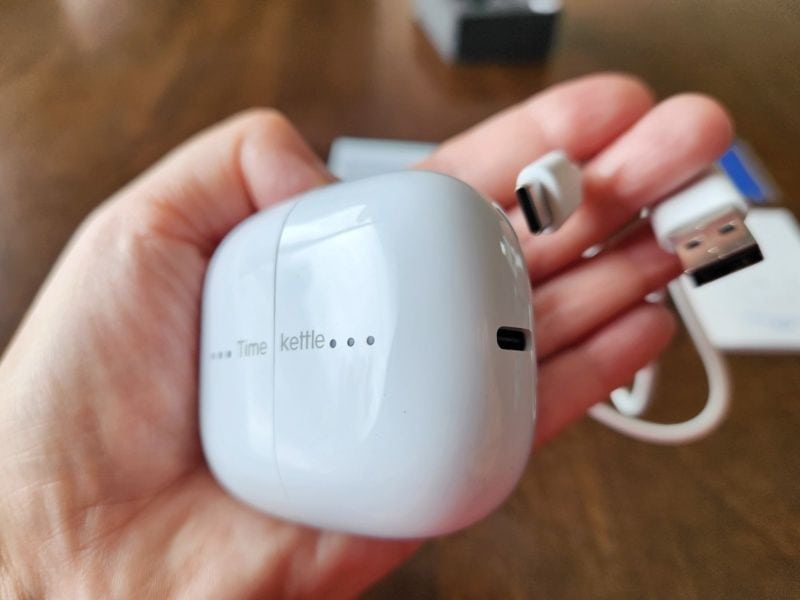 Holding the Timekettle M3 translator earbuds and USB cable