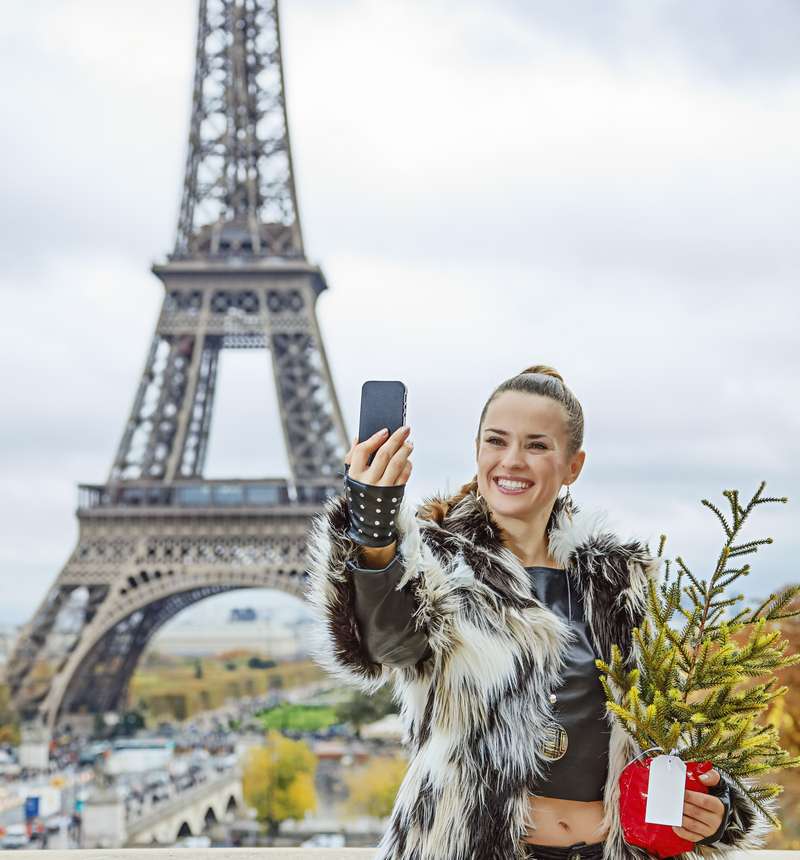 Stylish young woman with Christmas tree taking selfie in Paris
