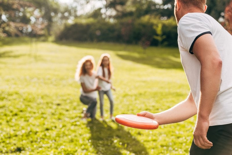 dad throwing Frisbee to mom and daughter in back yard