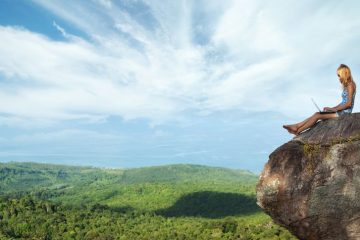 woman on laptop on rock overlooking mountians