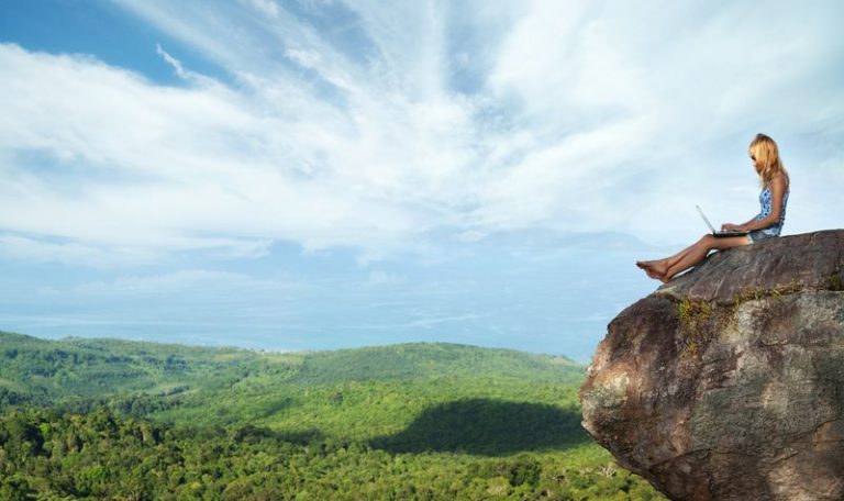 woman on laptop on rock overlooking mountians