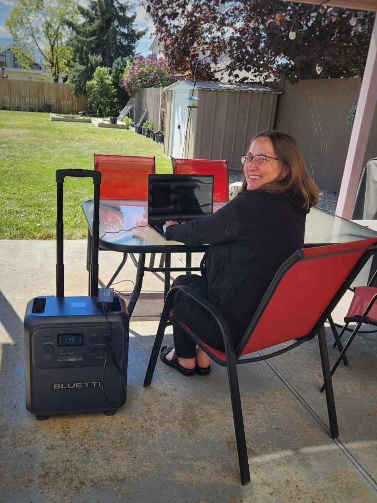 BLUETTI Elite 400 outside on patio overlooking back yard charging laptop woman smiling
